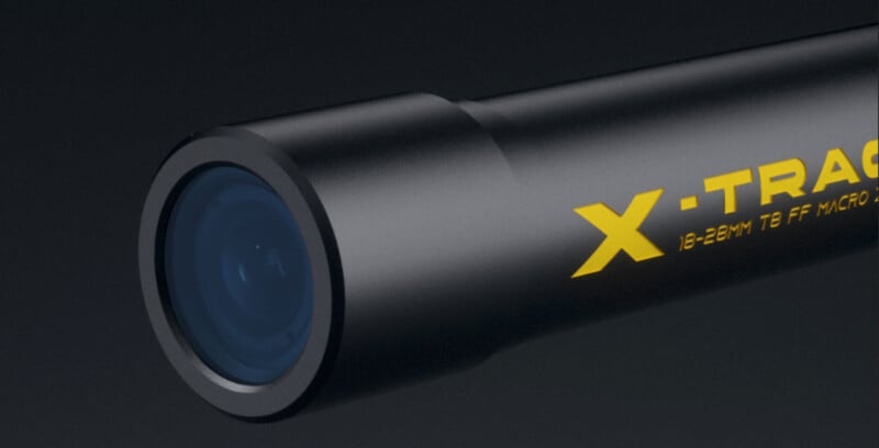 Close-up of a black cylindrical camera lens with blue-tinted glass, featuring the yellow text "X-TRAC" and specifications "18-28MM T8 FF MICRO" on its side, against a dark background.