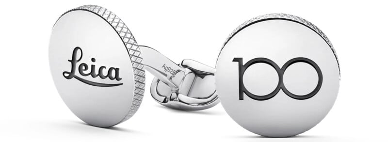 Silver cufflinks with textured edges. One displays the "Leica" logo, and the other shows the number "100" in a sleek, modern font.