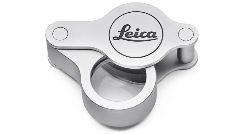 Silver Leica magnifying lens cap with a glass center, designed for camera lenses. The cap features the Leica logo engraved on the metal surface.