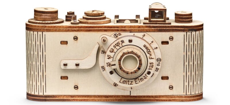 Wooden model of a vintage camera with detailed engravings, featuring various dials and a lens labeled "Leitz Elmar." The camera is simple and artisanal, displaying intricate craftsmanship.