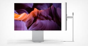 A sleek, modern computer monitor displays a vivid image of purple and orange rock formations. The side view shows the monitor's slim profile and minimalist stand design against a white background.