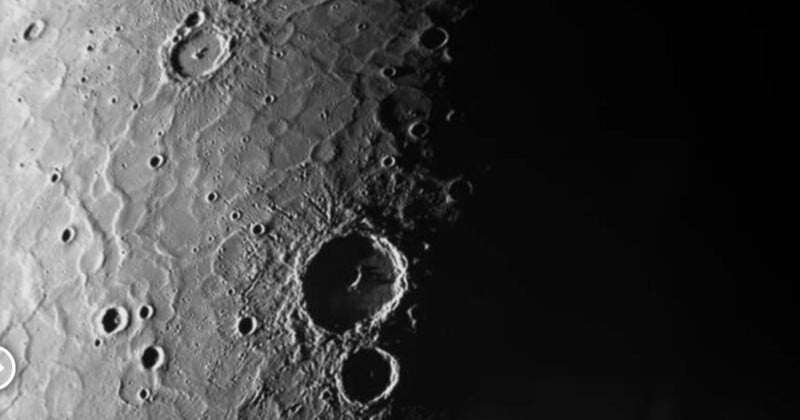 A detailed grayscale image of the Moon's surface, featuring numerous craters and a stark contrast between illuminated and shadowed areas. Several large craters are prominent in the center-left, highlighting the rugged lunar terrain.