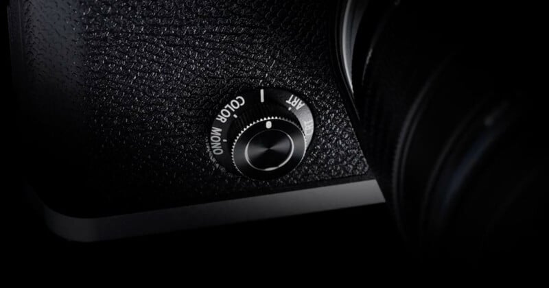 Close-up of a camera's mode dial, positioned at the corner of the device. The textured surface shows options for "Color" and "Mono" settings, with "ART" partially visible. The dial is shiny and metallic, contrasting with the dark camera body.