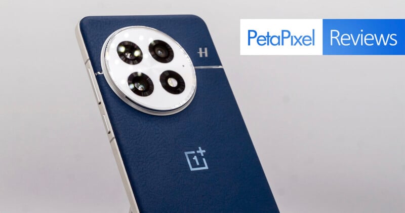 A smartphone with a blue back cover featuring a round triple-camera setup labeled with a small "H." The OnePlus logo is visible beneath the camera. A "PetaPixel Reviews" banner is in the top right corner.