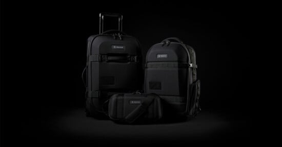 A set of three sleek black travel bags on a dark background: a suitcase with wheels and handle, a large backpack, and a small shoulder bag. They feature durable materials and a minimalist design with subtle branding.