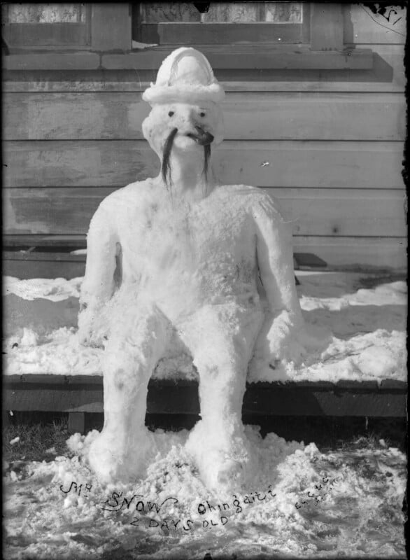 A snow sculpture of a seated figure with a hat and facial features, including a dark mustache, is positioned outdoors. Text at the bottom reads "MY SNOW BINGAL" with additional notes. A wooden building is in the background.