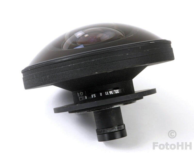 A fisheye camera lens with a wide, dome-shaped front element. It has a black exterior and manual focus markings on the barrel. The lens is positioned diagonally against a plain white background.