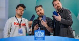 Three men stand holding smartphones, examining them with curious expressions. They wear casual jackets and lanyards. A logo reading "PetaPixel" is displayed at the bottom of the image.