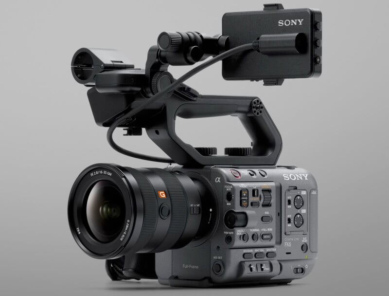 A professional Sony full-frame video camera with a lens, handle, and multiple control buttons, sits on a plain gray background. It features a microphone mount and an attached monitor on top.