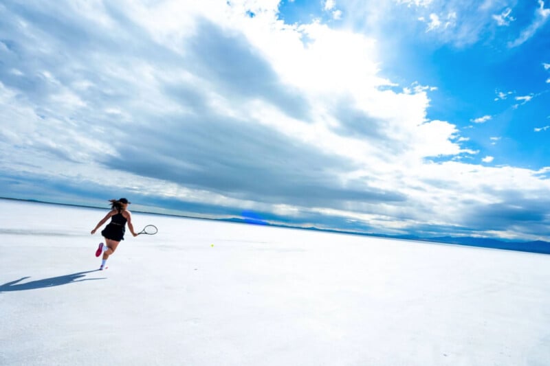 A person in athletic attire runs with a tennis racket across⁤ a vast,‌ white, open landscape under a bright blue ‌sky with scattered clouds. The wide expanse⁢ suggests a salt ⁣flat, with distant mountains⁢ on the horizon.