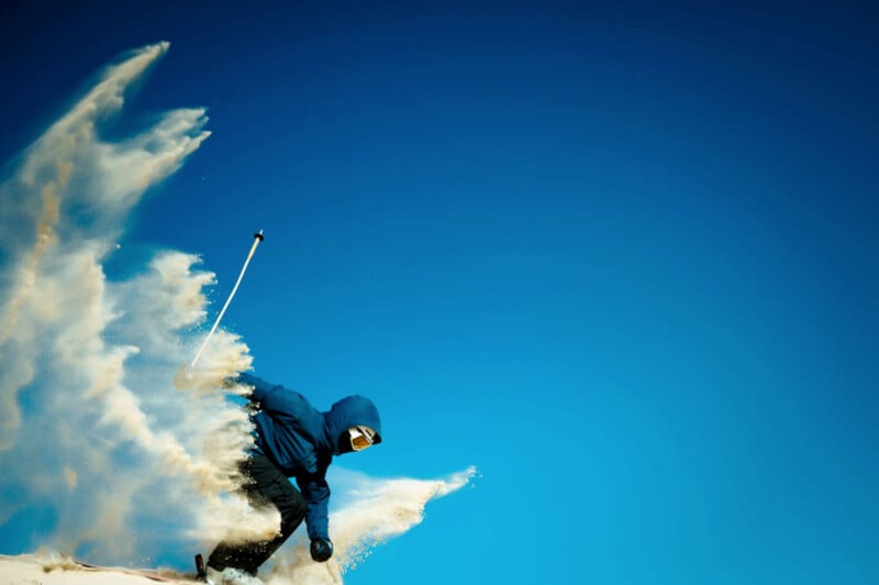 A skier​ in a blue⁤ outfit and goggles makes a sharp turn on a snowy slope, creating a spray of snow against a clear blue‌ sky.