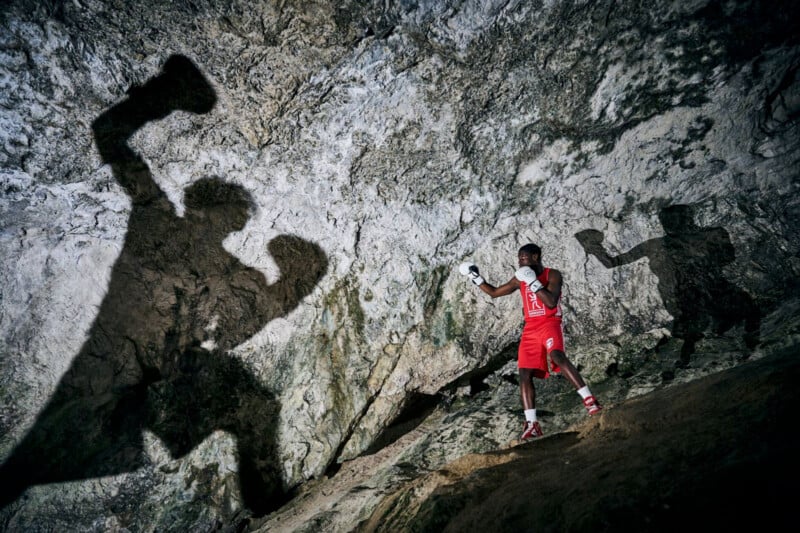 A boxer in red gear strikes a pose inside a rugged mountain cave, casting a dramatic shadow on the rocky wall. the dim lighting creates ⁤a striking silhouette effect, emphasizing the​ texture of the stone backdrop.