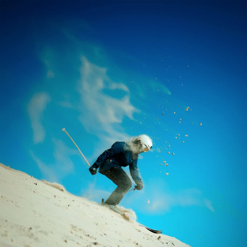 A​ skier wearing a helmet and‍ goggles glides down a sand dune under a clear blue sky. Sand sprays up behind‌ them, ⁤creating a ⁣dynamic and adventurous scene.