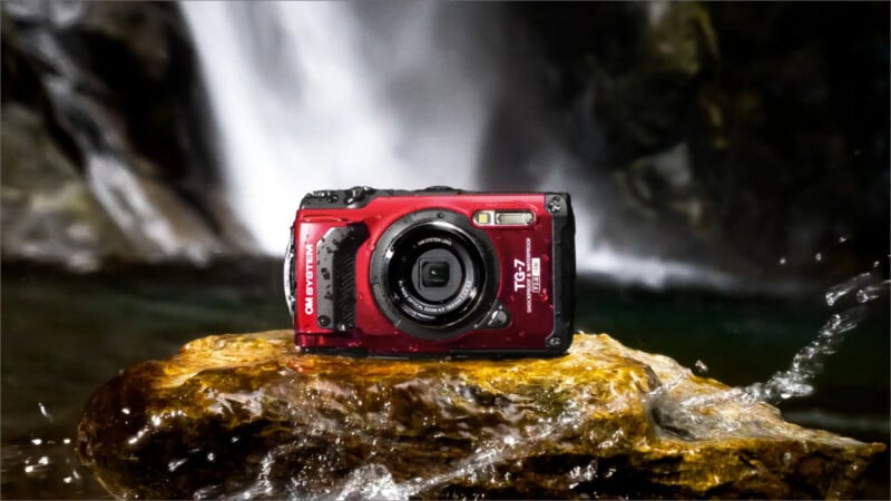 A rugged, red waterproof camera sitting on a wet rock with a waterfall in the background, capturing a sense of adventure and durability in an outdoor setting.