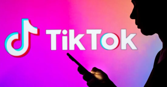 Silhouette of a person holding a smartphone against a colorful pink and purple background displaying the TikTok logo and text.