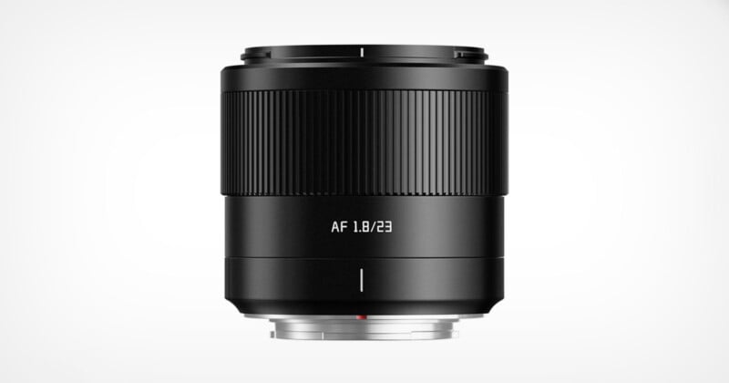 A black camera lens labeled "AF 1.8/23" is centered against a white background. The design features a textured focus ring and a smooth metal mount.