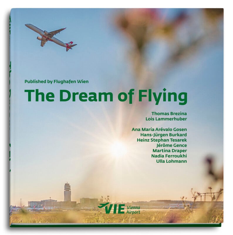 The cover of "The Dream of Flying," featuring an airplane in flight against a clear sky. In the foreground, blurred grass and flowers are visible. The book's author names and "Vienna Airport" logo are displayed below the title.