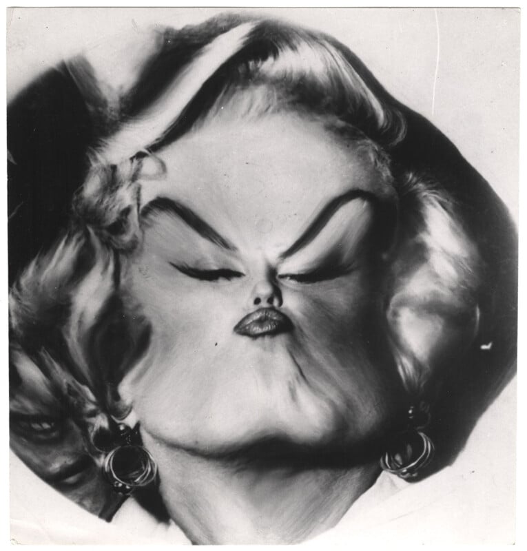 Black and white image of a person with distorted facial features, emphasizing exaggerated eyebrows, lips, and a puffed-out expression. The person has light, curly hair and is wearing large hoop earrings.