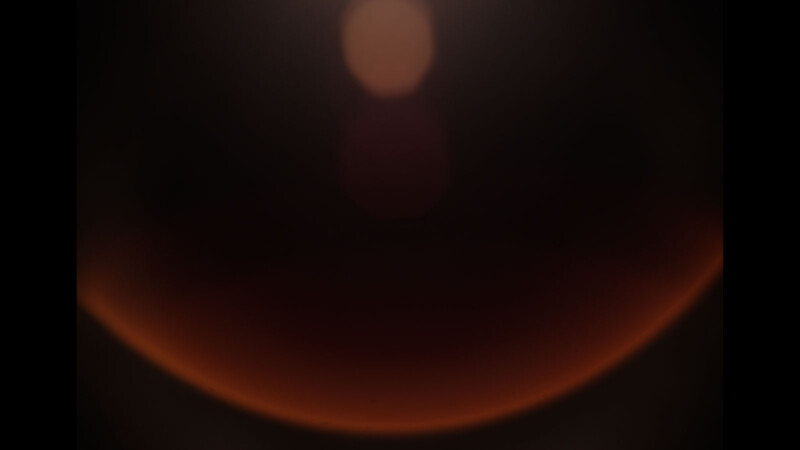 A dark, abstract image with a gradient suggesting a crescent-shaped orange glow at the bottom. Above it, several soft, circular, reddish light spots gradually fade into the dark background.