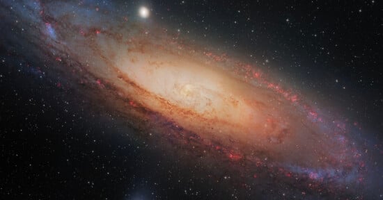 A stunning image of a spiral galaxy with a bright core surrounded by swirling stars and dust. The galaxy's arms exhibit pinkish-red regions, indicating star formation, set against a black starry background.