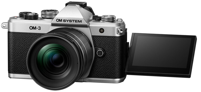 Silver OM System OM-3 camera with a black textured body, featuring an extended touchscreen display on the right. The camera lens is large and slightly angled, displaying a green tint on the glass. Various dials and buttons are visible on top.