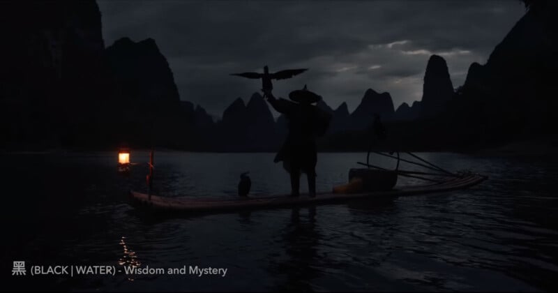 A person stands on a raft in a dark, mountainous lake, holding a bird with outstretched wings. A lantern glows on the raft, casting a soft light. Another bird stands nearby. Text reads: "黑 (BLACK) | WATER - Wisdom and Mystery.