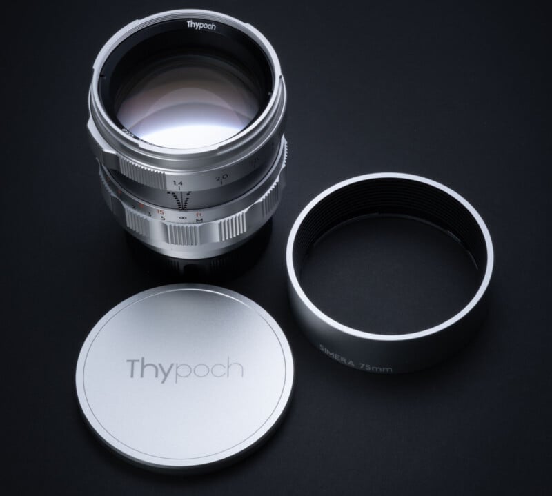 A silver camera lens with the brand name "Thypoch" is displayed on a dark surface. The image shows the lens alongside its cap and an additional ring labeled "CHIMERA 75mm.