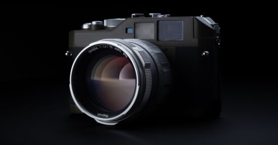 A close-up of a modern digital camera with a large lens, set against a black background. The camera features a metallic finish with various buttons and dials on the top. Reflections are visible on the lens surface.