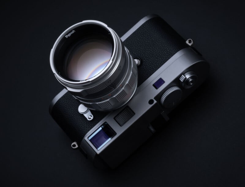 A black and silver camera with a large lens is set against a dark background. The camera features various buttons, dials, and a viewfinder. The lens is prominently displayed, reflecting light.