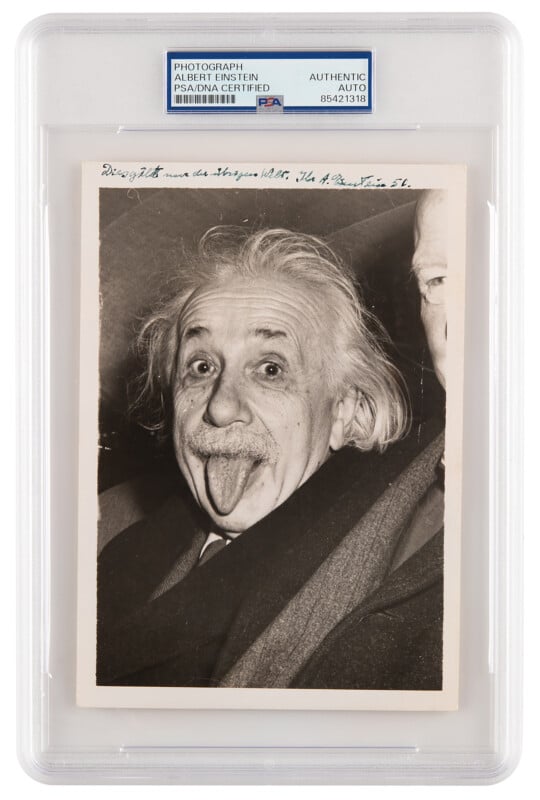 Black and white photo of a man with wild hair sticking out his tongue. The photo is encased in a protective display labeled "PHOTOGRAPH AUTHENTIC AUTO," with handwritten text above the image.