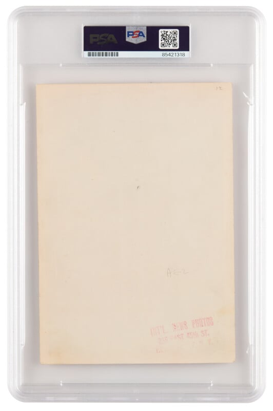 A vintage photograph encased in a PSA protective slab with a barcode and labels at the top. The back of the photo has a red stamp with text, indicating the photo studio's address in New York. The surface of the photo's back is mostly blank.