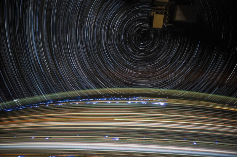 A stunning long-exposure photograph captures star trails forming circular patterns in the night sky, with the curvature of Earth illuminated by city lights and a prominent space station feature in the upper right corner.