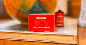 A red box of Harman Red ISO 125 Redscale film sits on a closed book with a blurred background. Next to it is a film roll, also blurred.