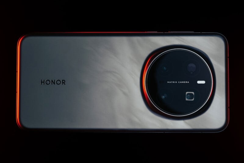 A smartphone with a metallic finish and a large round camera module on the back, labeled with "Honor" and "Matrix Camera." The device is set against a dark background with orange lighting highlighting its edges.