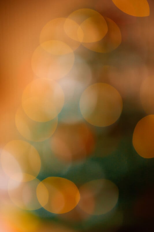 A blurred image featuring soft, overlapping circles of warm lights in shades of orange, yellow, and green, creating an abstract and dreamy bokeh effect against a softly colored background.