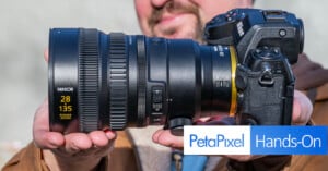 A person holding a Nikon camera with a large Nikkor 28-135mm zoom lens. The text "PetaPixel Hands-On" is overlaid in the bottom right corner.