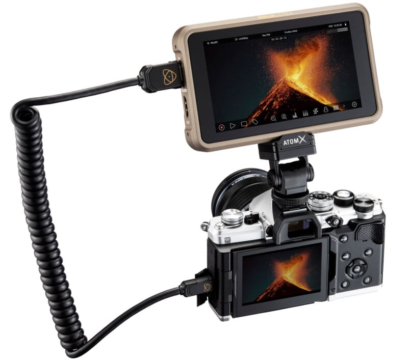 A digital camera connected to an external screen displaying an erupting volcano. The screen is mounted on top of the camera, and both show the same image. Cables tether the devices together.