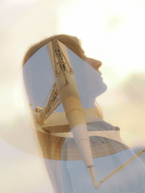 A double-exposure image of a woman's silhouette combined with a large telescope structure. The telescope's metallic framework is prominently visible against a pale sky, blending with the woman's profile.