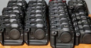 Rows of Canon EOS-1D cameras are neatly arranged on a wooden surface, with lenses detached. The cameras are positioned facing forward, showcasing their brand and model. The setup appears organized, possibly for sale or inventory.