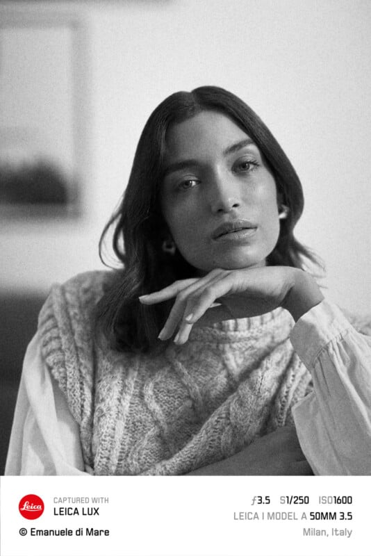 Black and white portrait of a person with long hair, resting their chin on their hand. They wear a knit vest over a blouse. The camera settings and location details are shown at the bottom.