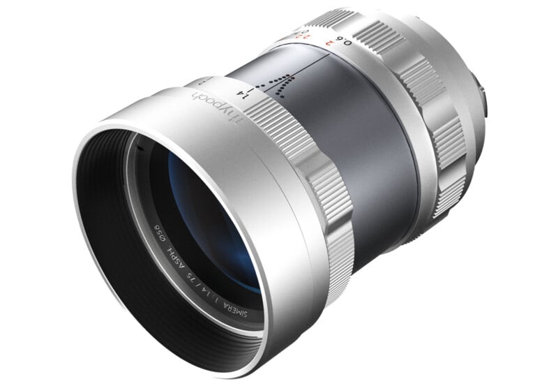 A silver camera lens with a wide front element and textured focus ring, featuring marked numbers and a smooth metallic finish. The lens is angled, capturing both the front and side view, highlighting its sleek design.