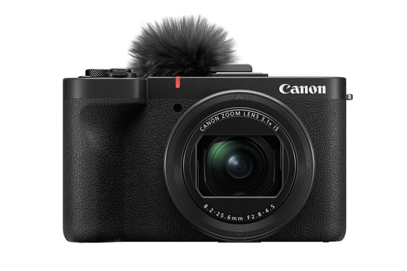 Front view of a Canon digital camera with a lens labeled "Canon Zoom Lens 3.1-15," featuring a built-in microphone with a windscreen on top. The camera body is black and has textured grips.