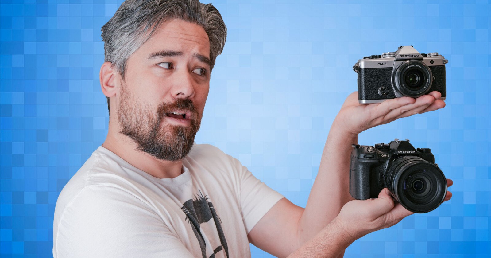 A man with gray hair and a beard holds two cameras, one in each hand, while looking at them. The background is a gradient of blue squares. He wears a white t-shirt.