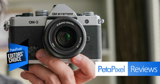A person holds an OM System OM-3 camera facing the viewer. The image features "Petapixel Editors' Choice" and "Petapixel Reviews" banners in the foreground.