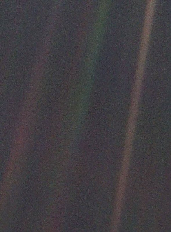 Faint colored stripes cross a dark background, with a tiny pale blue dot visible in one of the stripes. This image is known as the "Pale Blue Dot," a photograph of Earth taken by the Voyager 1 spacecraft from a distance of about 3.7 billion miles.