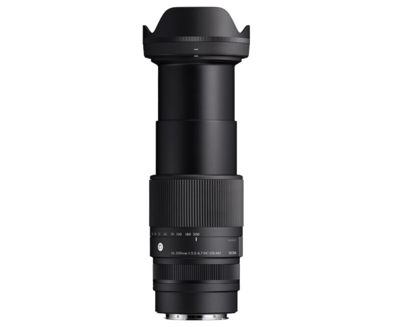 A black camera lens with a hood, extended and showing the zoom range marked on the barrel. The brand name is visible near the base, with numbers indicating focal lengths. The design is sleek and cylindrical.