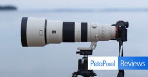 A large telephoto camera lens mounted on a tripod is shown. The lens is attached to a camera, and the setup is positioned to capture distant images. The word "PetaPixel" appears in blue alongside the word "Reviews" in white against a blue background.