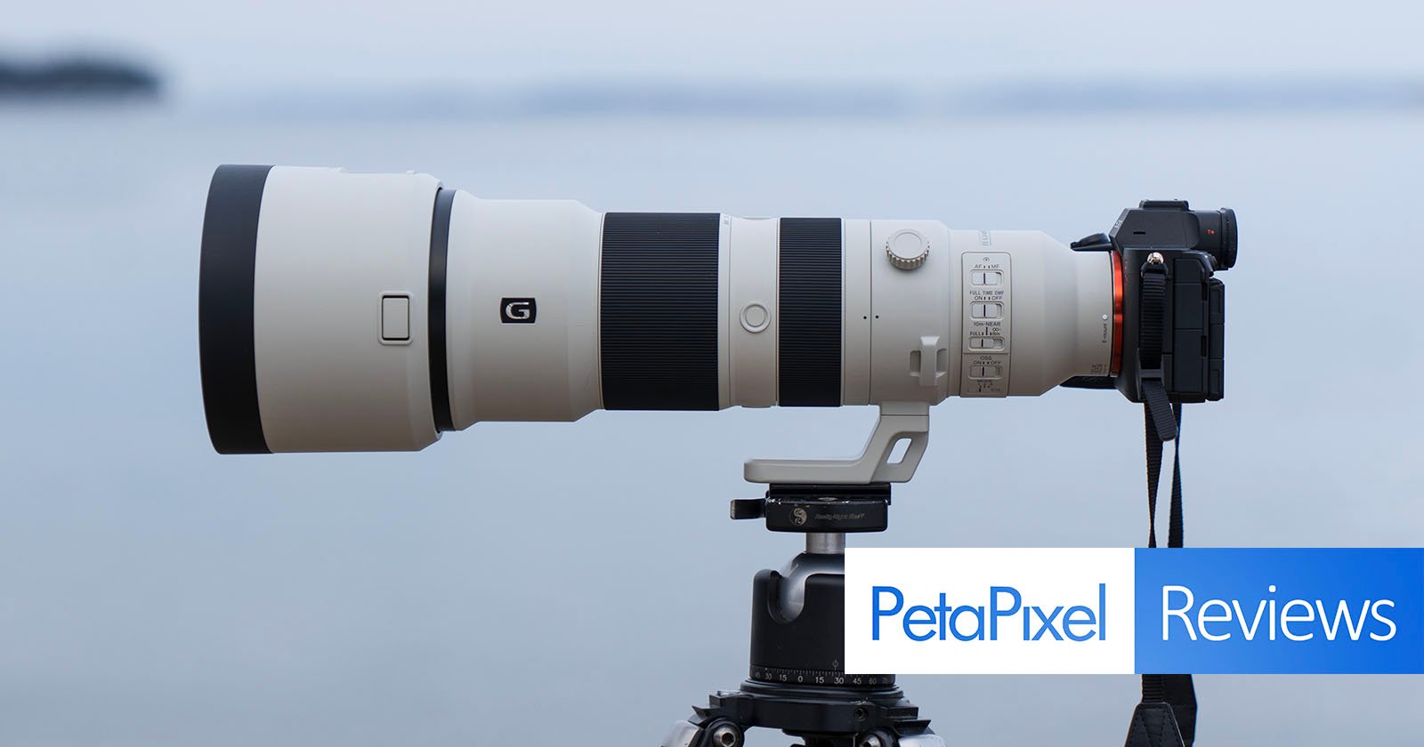 A large telephoto camera lens mounted on a tripod is shown. The lens is attached to a camera, and the setup is positioned to capture distant images. The word "PetaPixel" appears in blue alongside the word "Reviews" in white against a blue background.