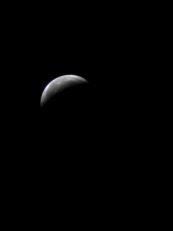 A crescent moon in the night sky with its illuminated part visible at the top, set against a black background.