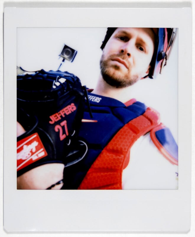 Baseball player in catcher's gear, holding a mitt with "Jeffers 27" written on it, looking at the camera. The image is a close-up Polaroid-style shot.